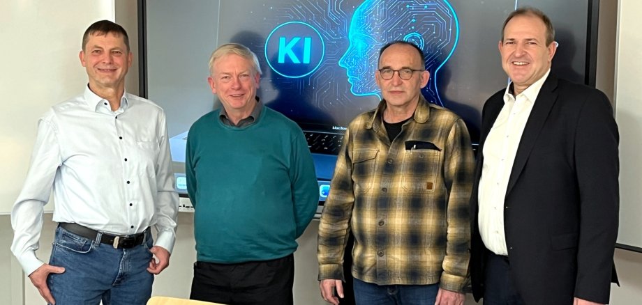 The photo shows the aforementioned people standing next to each other in front of the screen in the media room and looking into the camera.