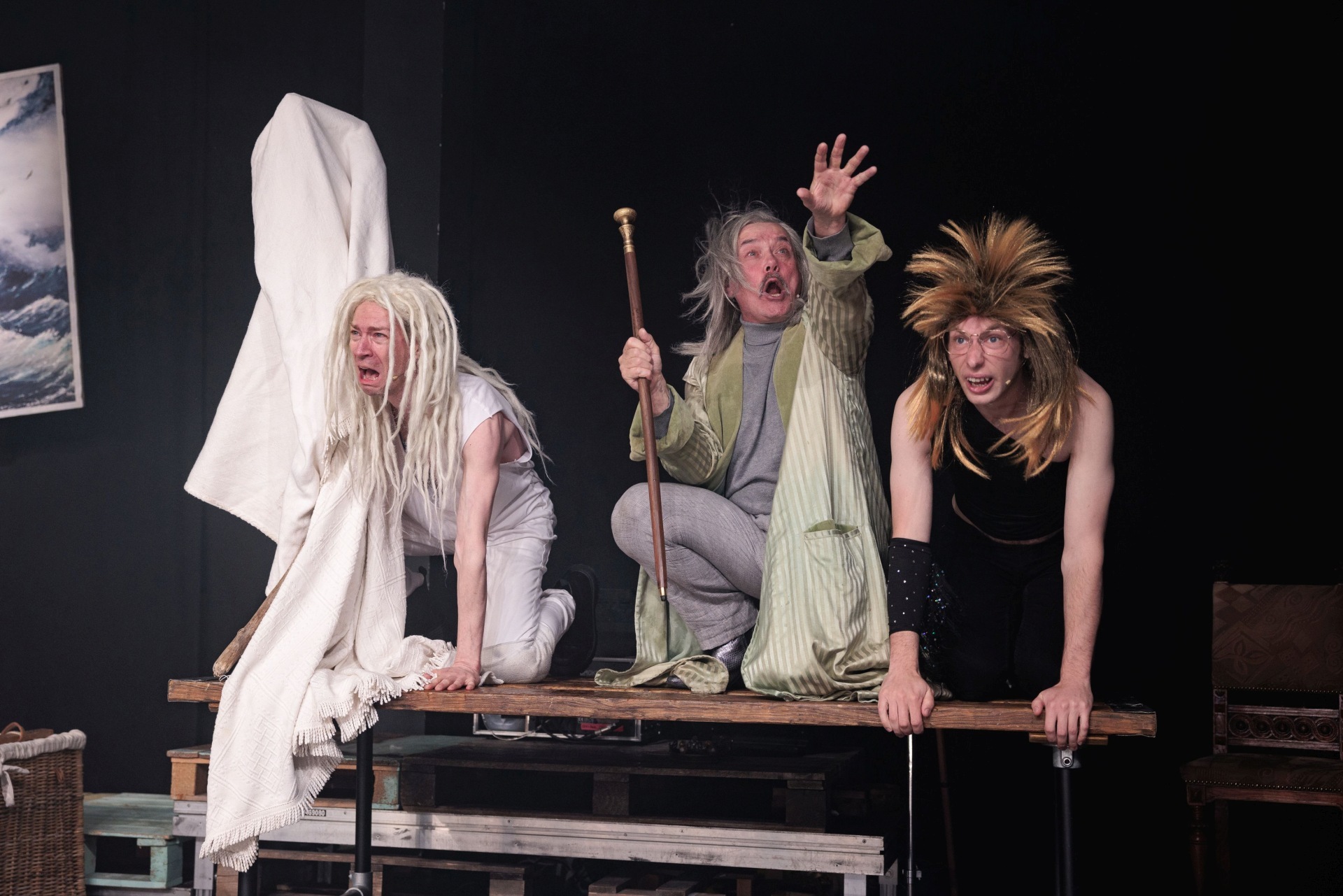 The photo shows three actors in costume kneeling on a table.