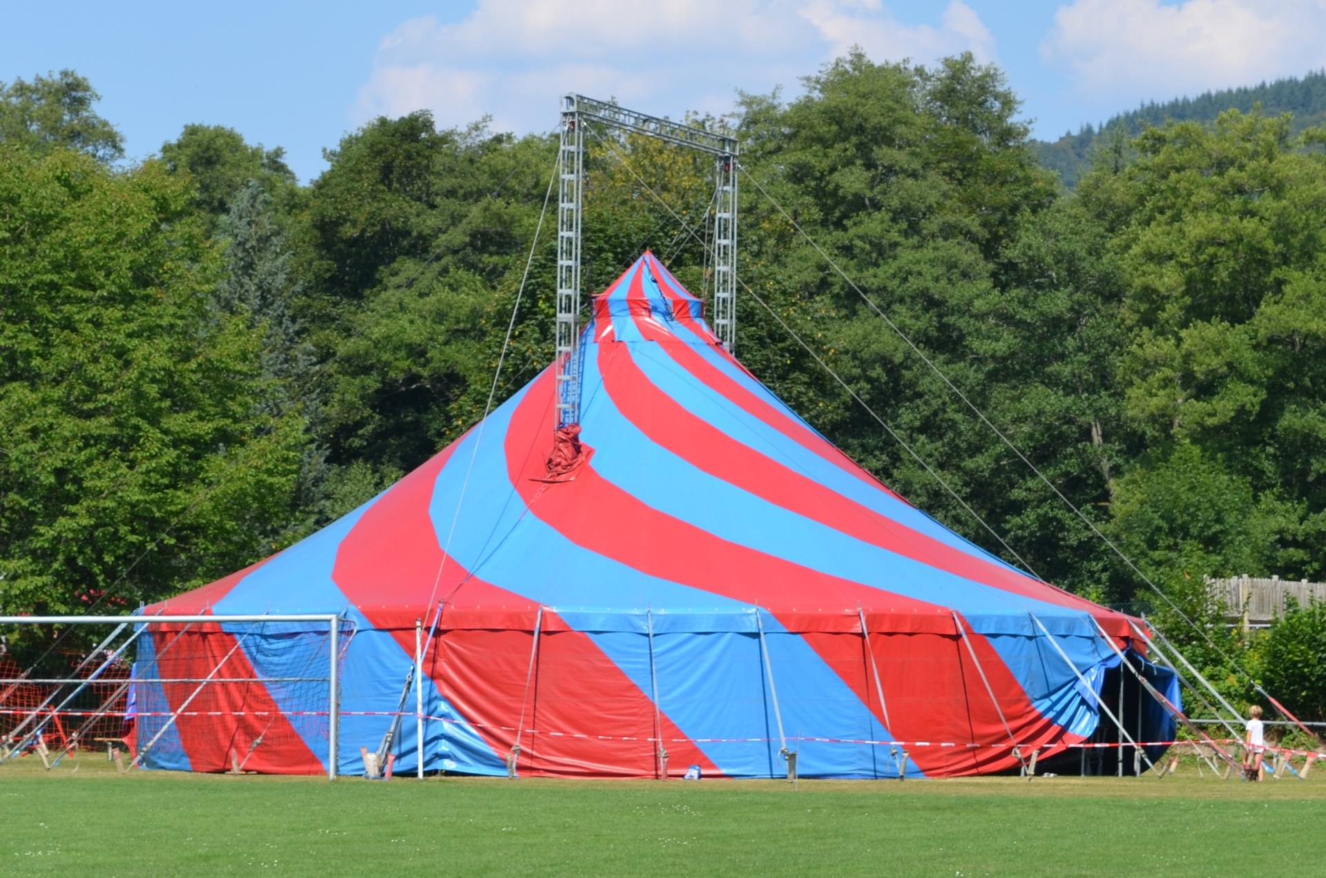 The photo shows a large, blue and red striped circus tent standing on a meadow.