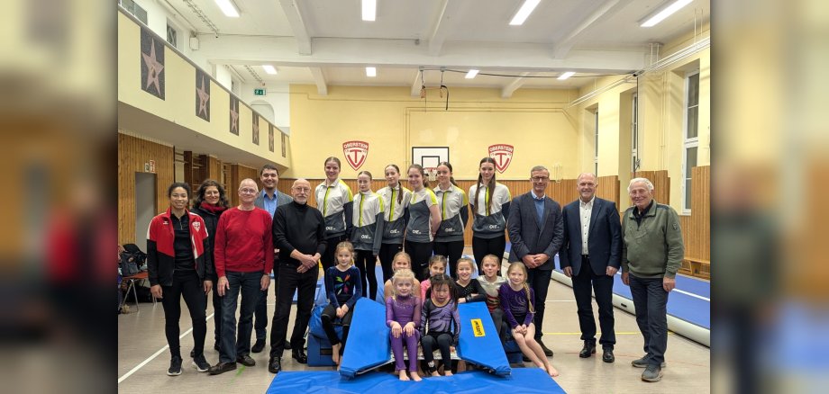 The photo shows the people mentioned. They are standing on gym mats in the lower gym of the municipal theater. The new LED lights can be seen on the ceiling.