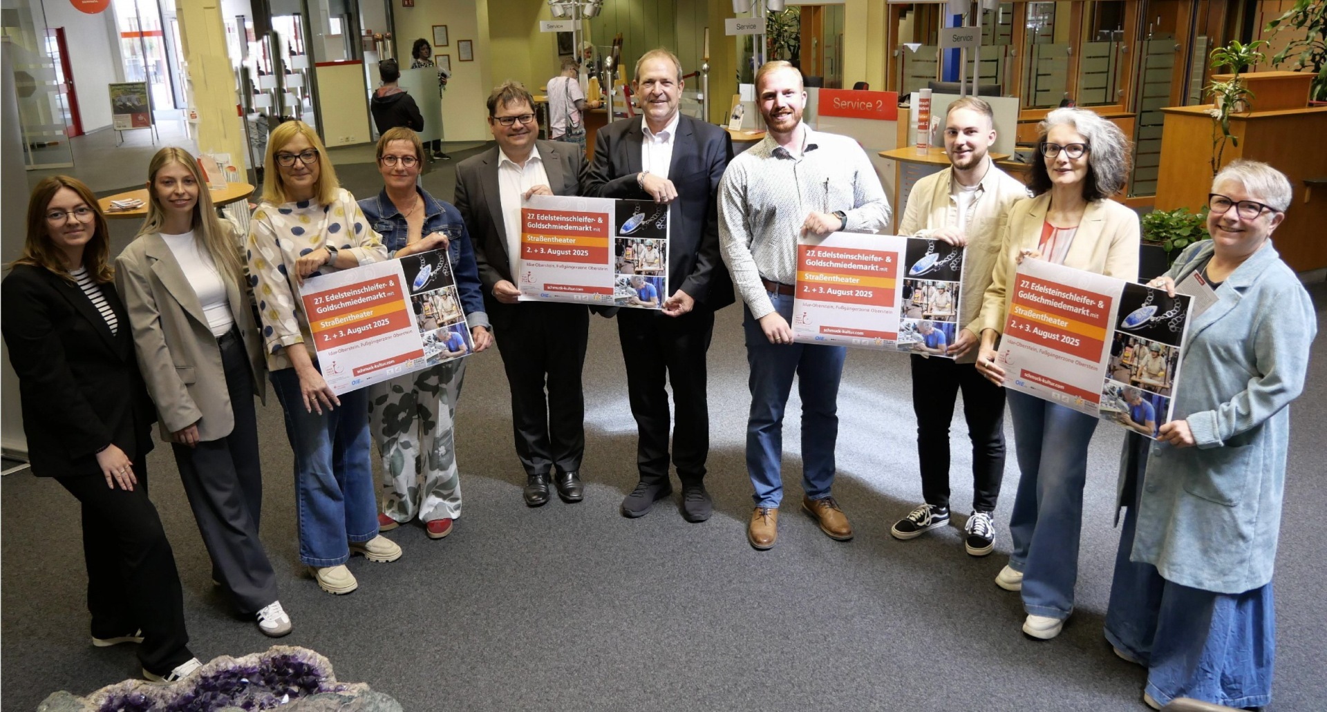 The photo shows the organizers and sponsors standing next to each other in the KSK cashier's hall and holding posters for the event up to the camera.