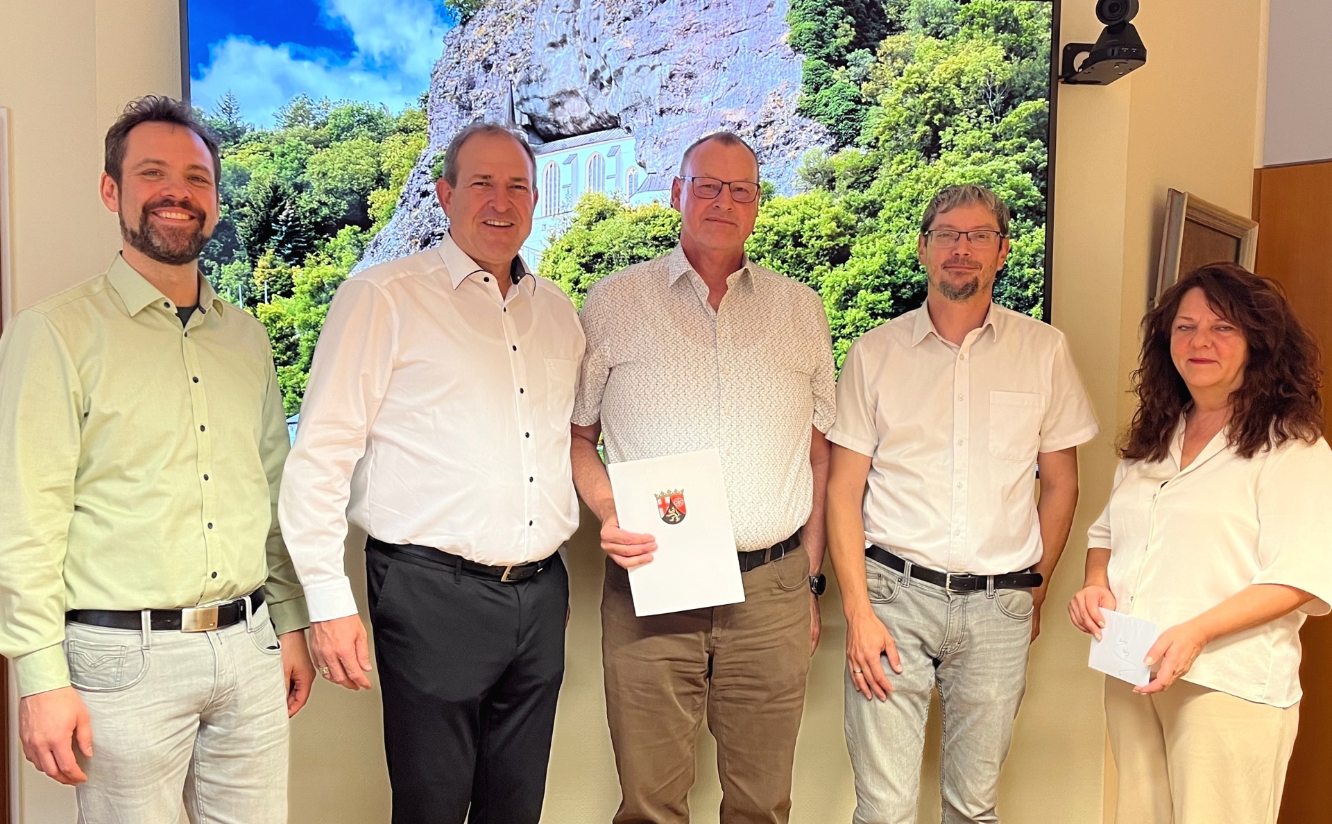 The photo shows the aforementioned people standing next to each other in the mayor's meeting room and looking into the camera. Markus Petry stands in the middle and holds the certificate of thanks in his hands.