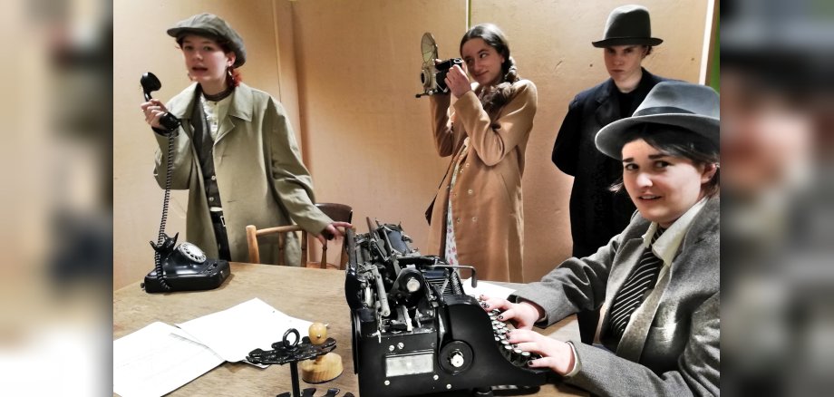 The photo shows a scene with four actors and actresses dressed in 1920s-style costumes.