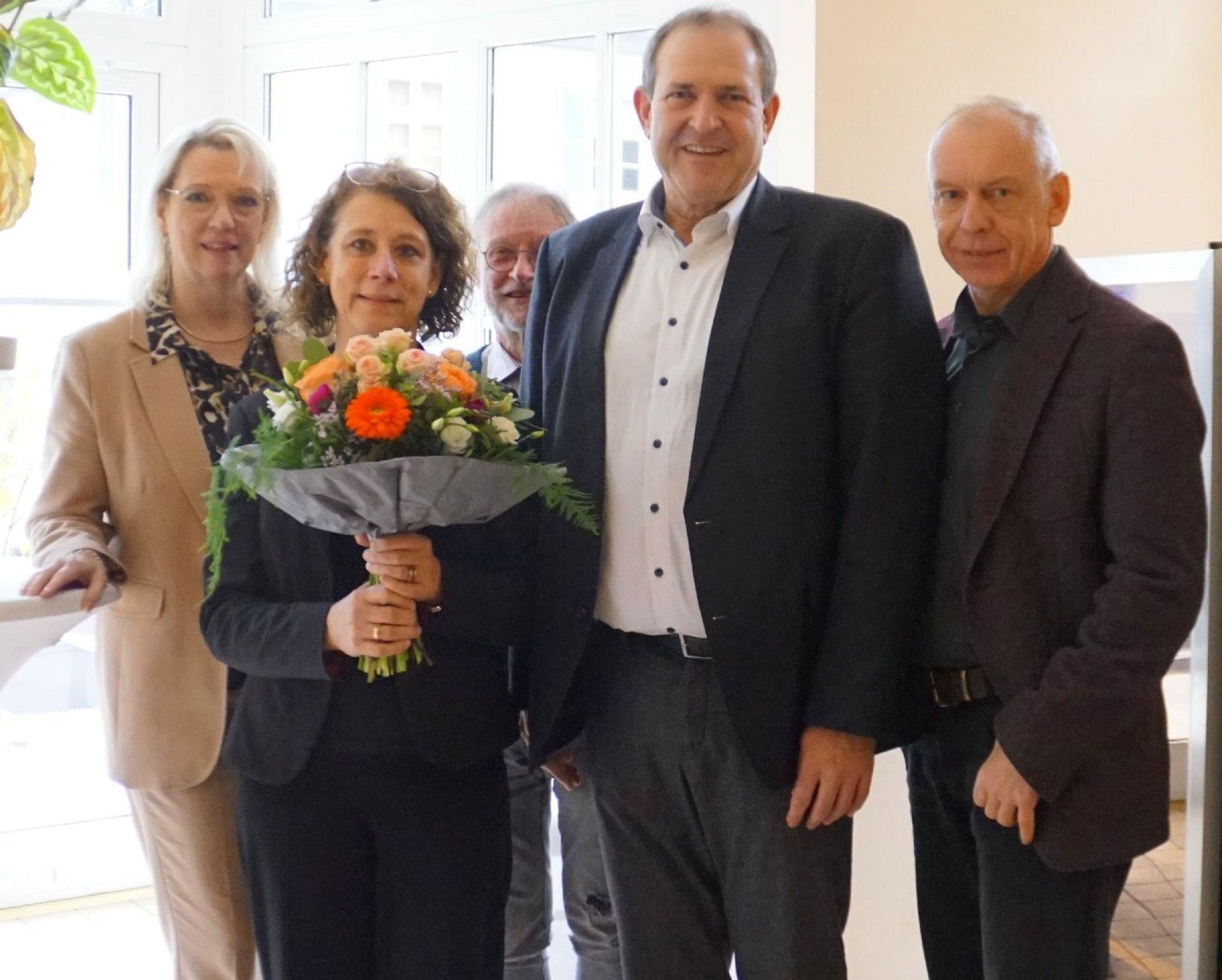 The photo shows the people mentioned. They are standing next to each other and looking into the camera. Eva Grosser is holding a bouquet of flowers.