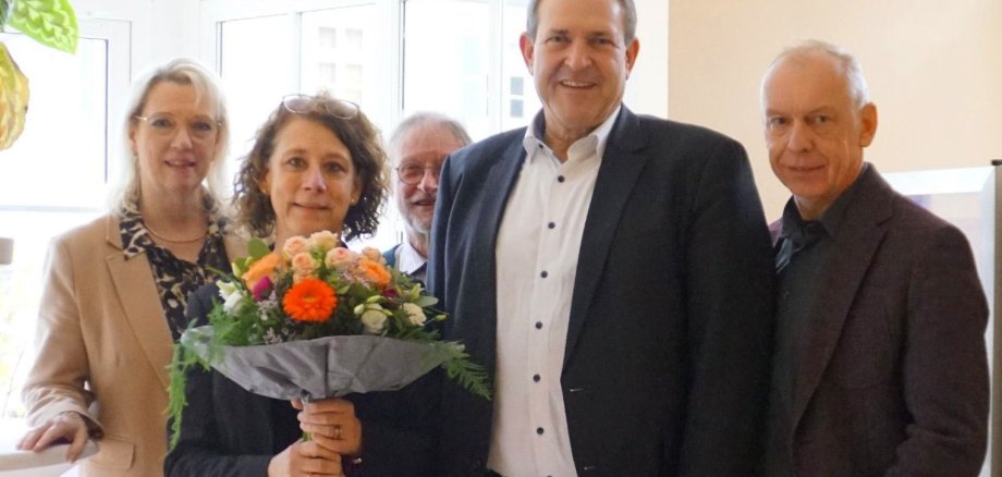 The photo shows the people mentioned. They are standing next to each other and looking into the camera. Eva Grosser is holding a bouquet of flowers.