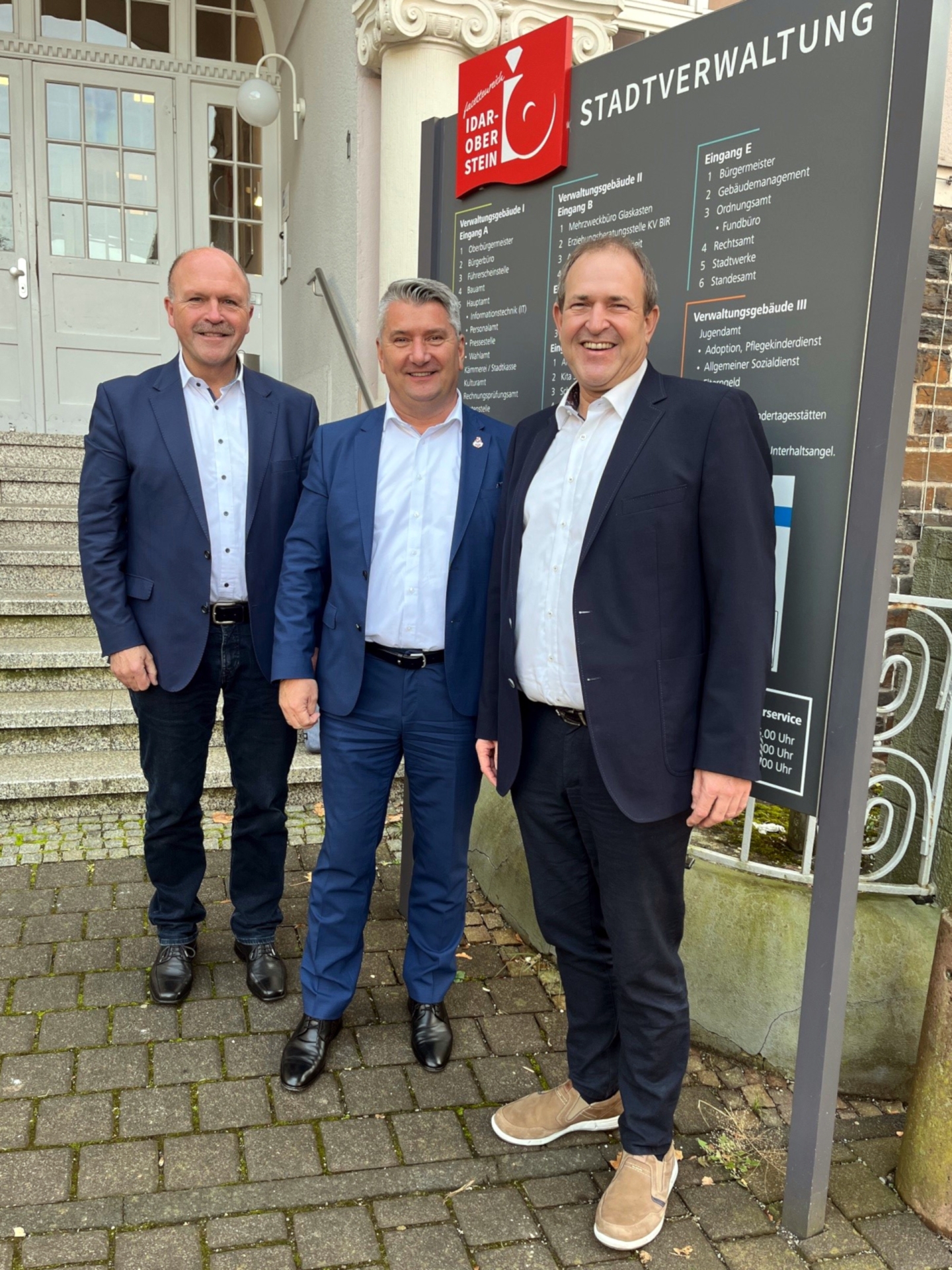The photo shows the above-mentioned people standing in front of the town hall by the town council's signpost board.