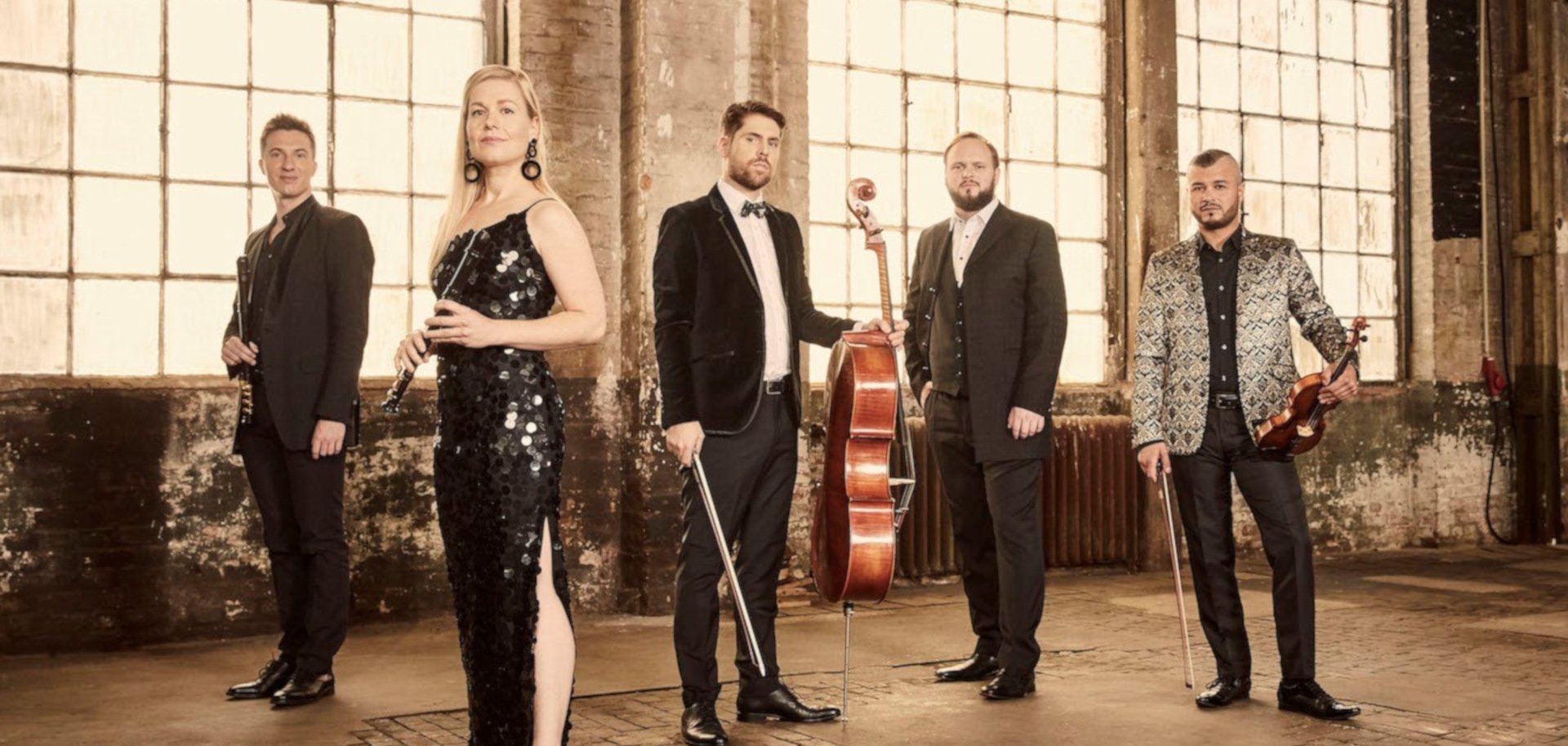 The photo shows the five musicians with their instruments in the ambience of an old factory.