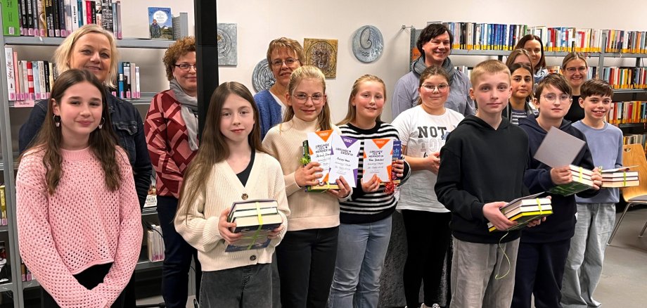 Organizer, jury and participants at the district reading competition 2025/2026. The group photo shows the aforementioned people in the city library. The readers are holding their certificates and book presents.