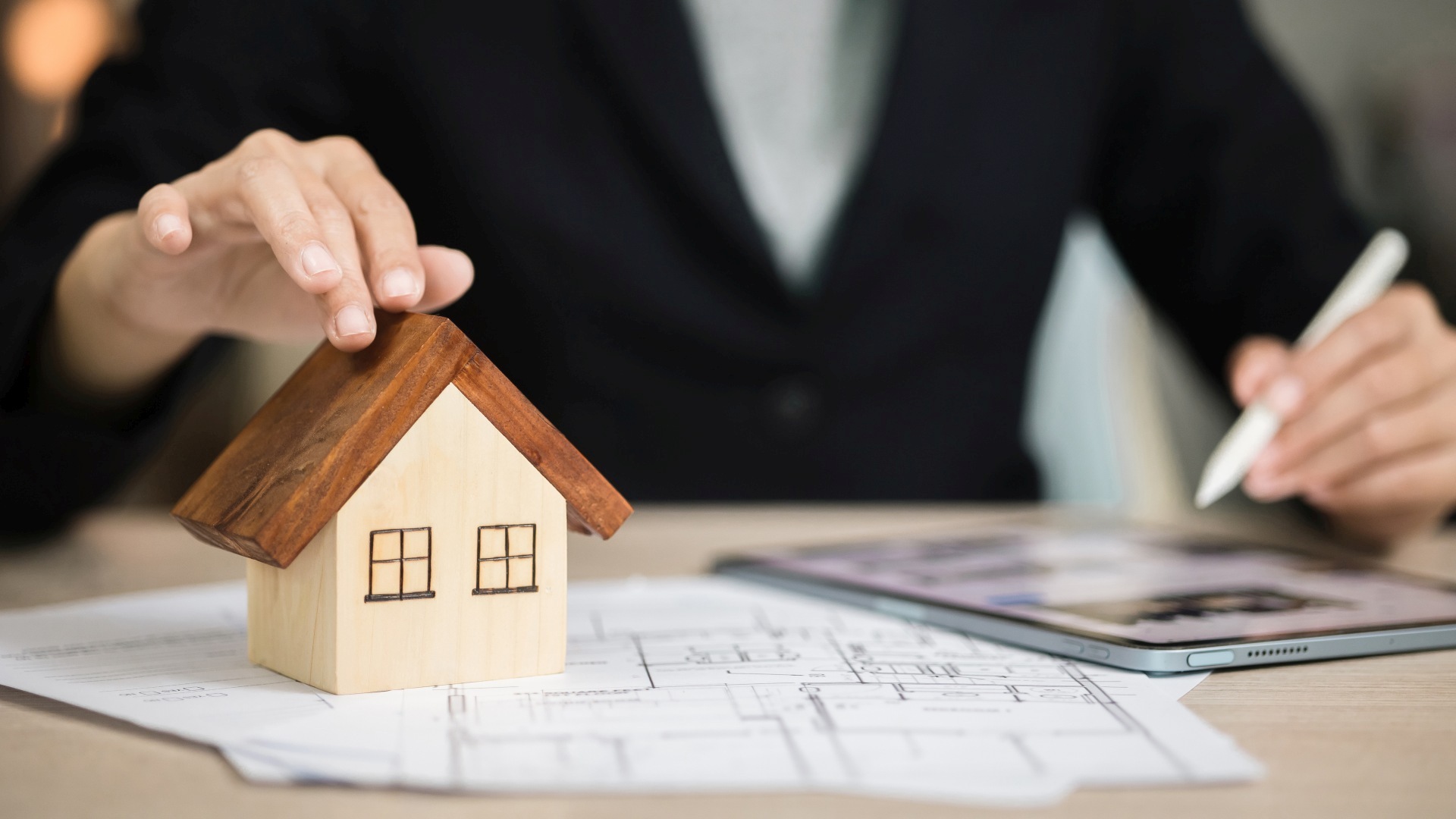 A person is sitting at a desk with a tablet and a model of a house.