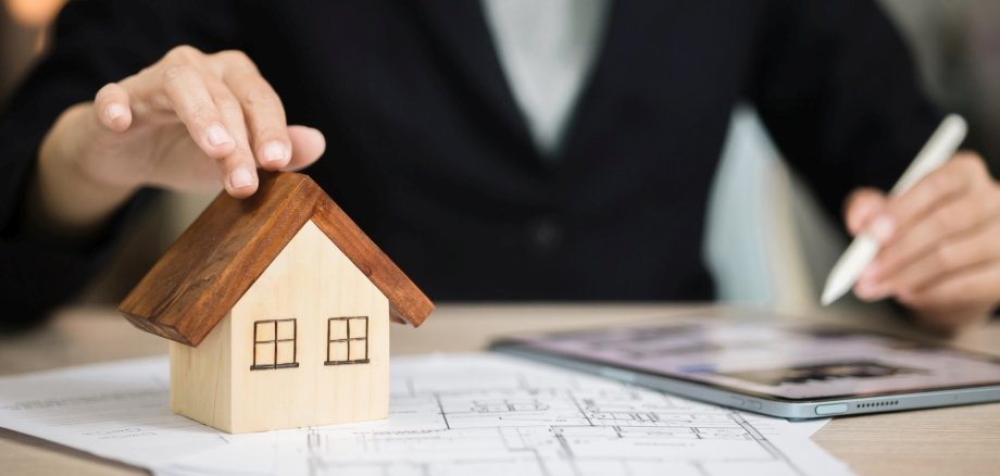 Building permits can now be applied for online in Idar-Oberstein. A person is sitting at a desk with a tablet and a model of a house.