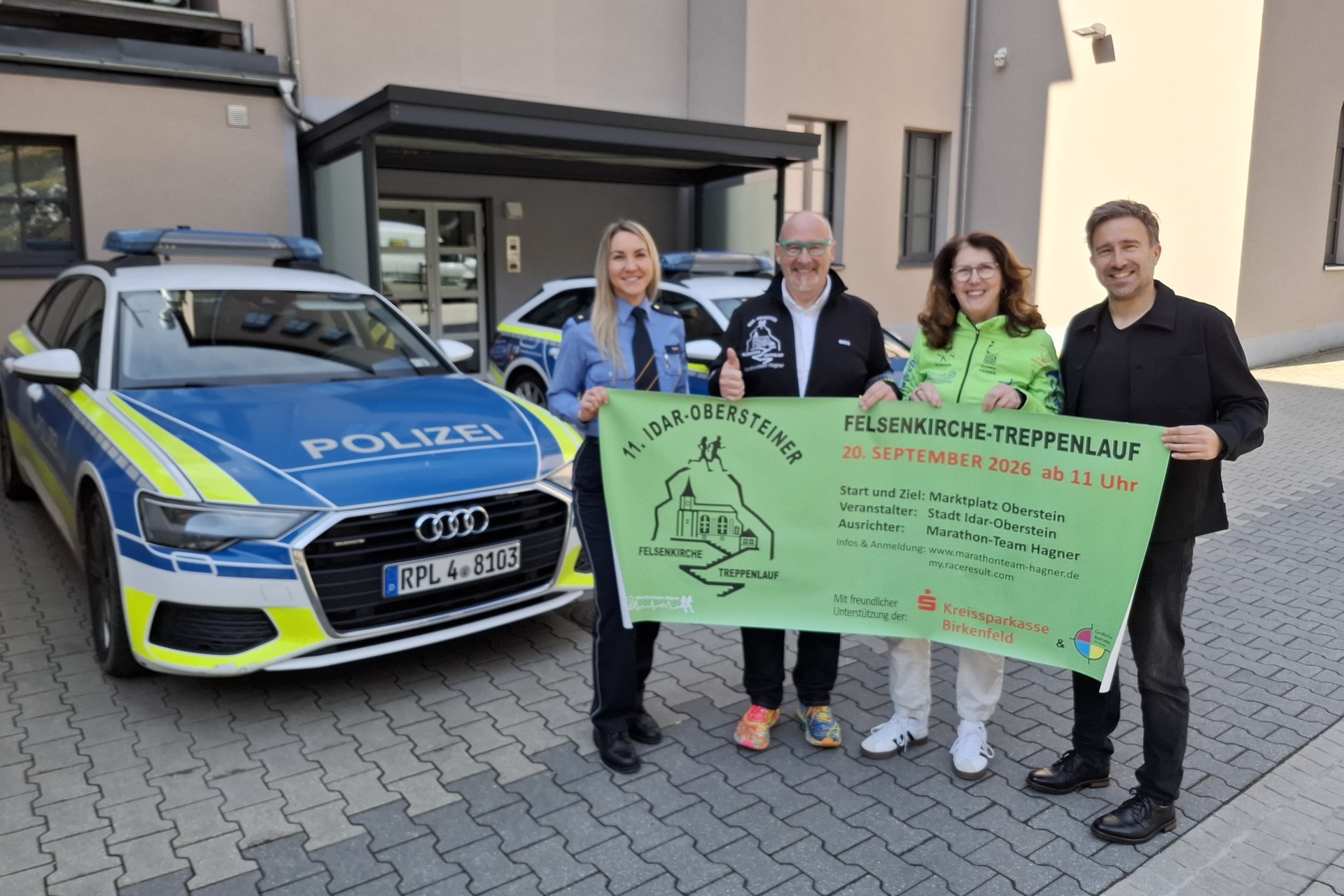 The photo shows the aforementioned people in the courtyard of the police station. They are standing in front of patrol cars and holding a banner of the stair run in front of the camera.
