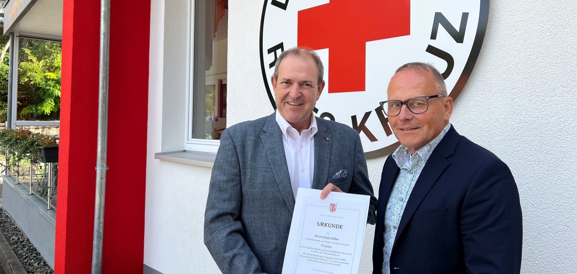 The photo shows the two people in front of the new building. Mayor Frühauf presents Jörg Schmitt with the certificate.