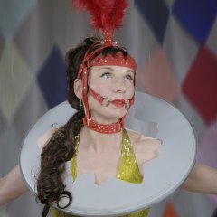 La photo montre la chanteuse dans un costume coloré avec une coiffure rouge. Elle porte autour du cou un tambour percé.