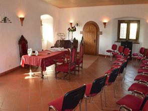 La photo montre une vue de la salle des mariages du château d'Oberstein. Sur la gauche de l'image, on peut voir le bureau de l'officier d'état civil, devant lequel se trouvent quatre chaises. Sur le côté droit de la photo, on peut voir d'autres chaises pour les participants.