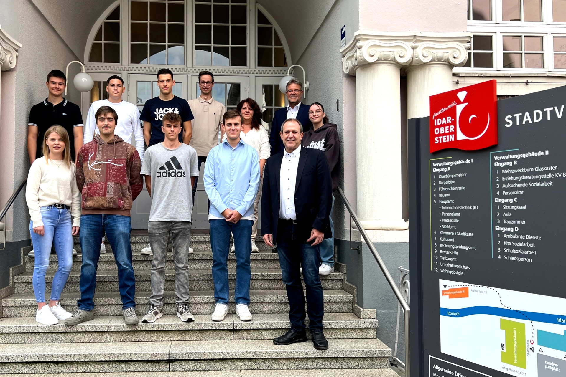 La photo montre les personnes mentionnées dans l'article, debout sur deux rangées dans les escaliers extérieurs devant l'hôtel de ville.