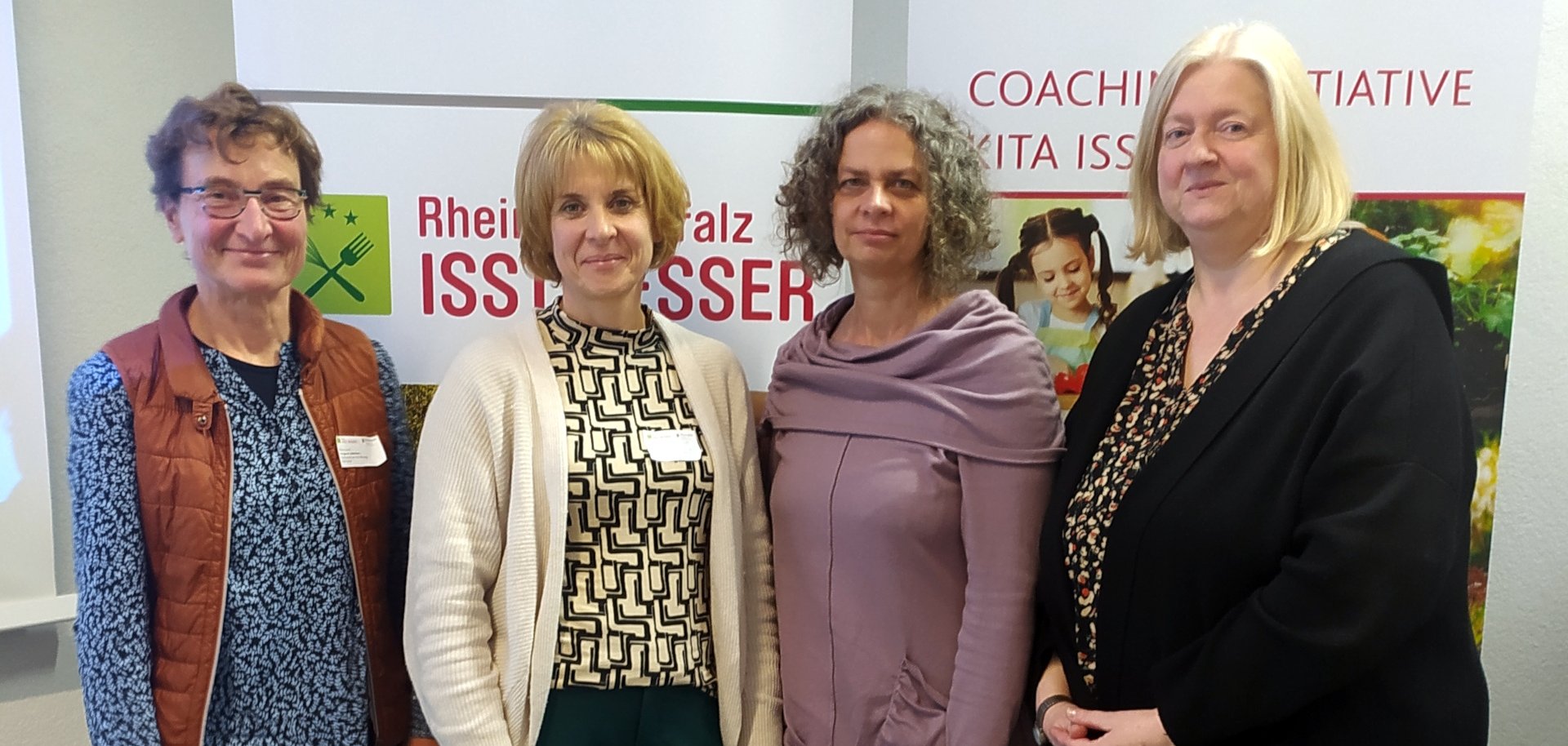 La photo montre les personnes mentionnées. Elles se tiennent devant deux rollups de l'initiative "kita isst besser".