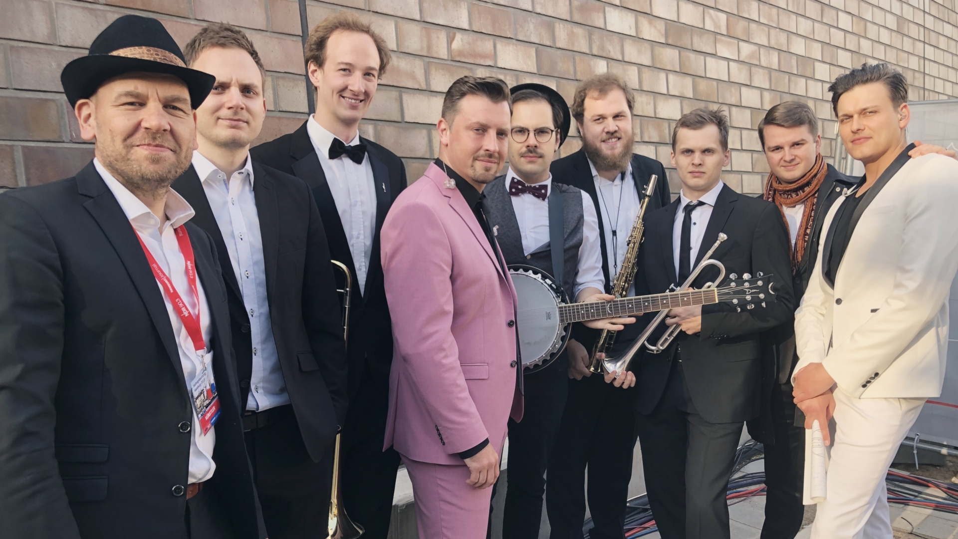 La photo montre les musiciens devant un mur de pierre.