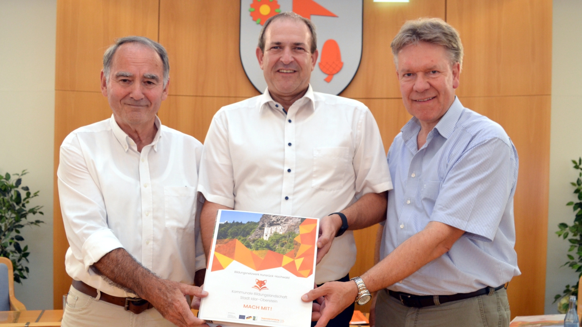 La photo montre, de gauche à droite, Peter Simon, adjoint au district, Alexander Hauck et Frank Frühauf, maire de la ville, tenant ensemble l'un des classeurs éducatifs devant l'objectif.