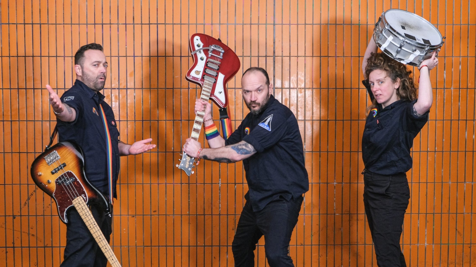 La photo montre les trois musiciens du groupe Raketen Erna avec leurs instruments devant un mur de carrelage.