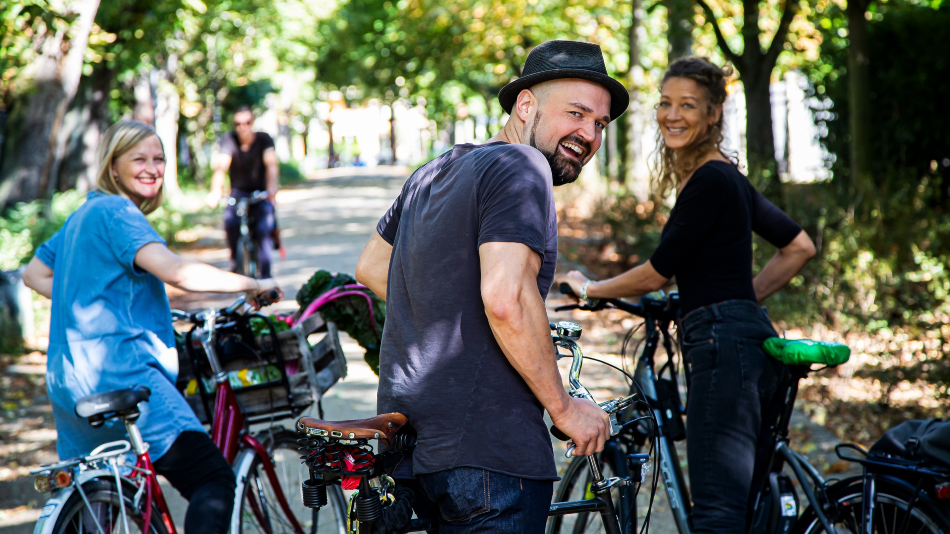 La photo montre trois cyclistes debout avec leurs vélos sur un chemin bordé d'arbres et regardant l'appareil photo.