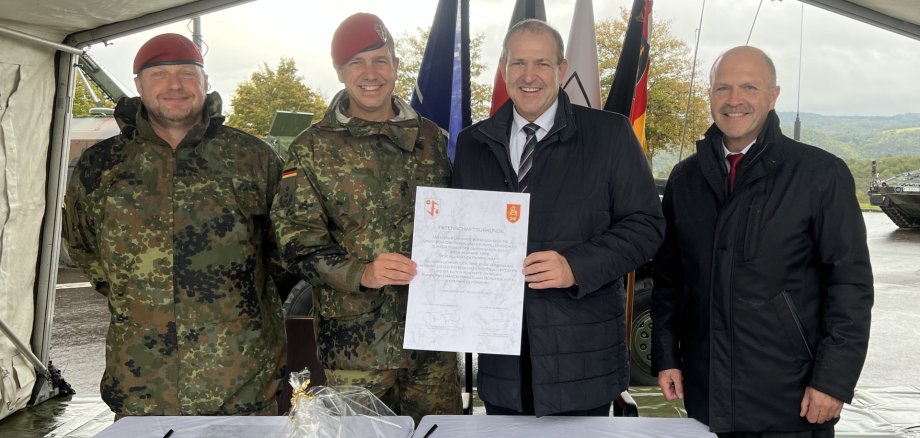 La photo montre les personnes mentionnées, le colonel Tuneke et le maire Frühauf tenant le certificat devant l'objectif.