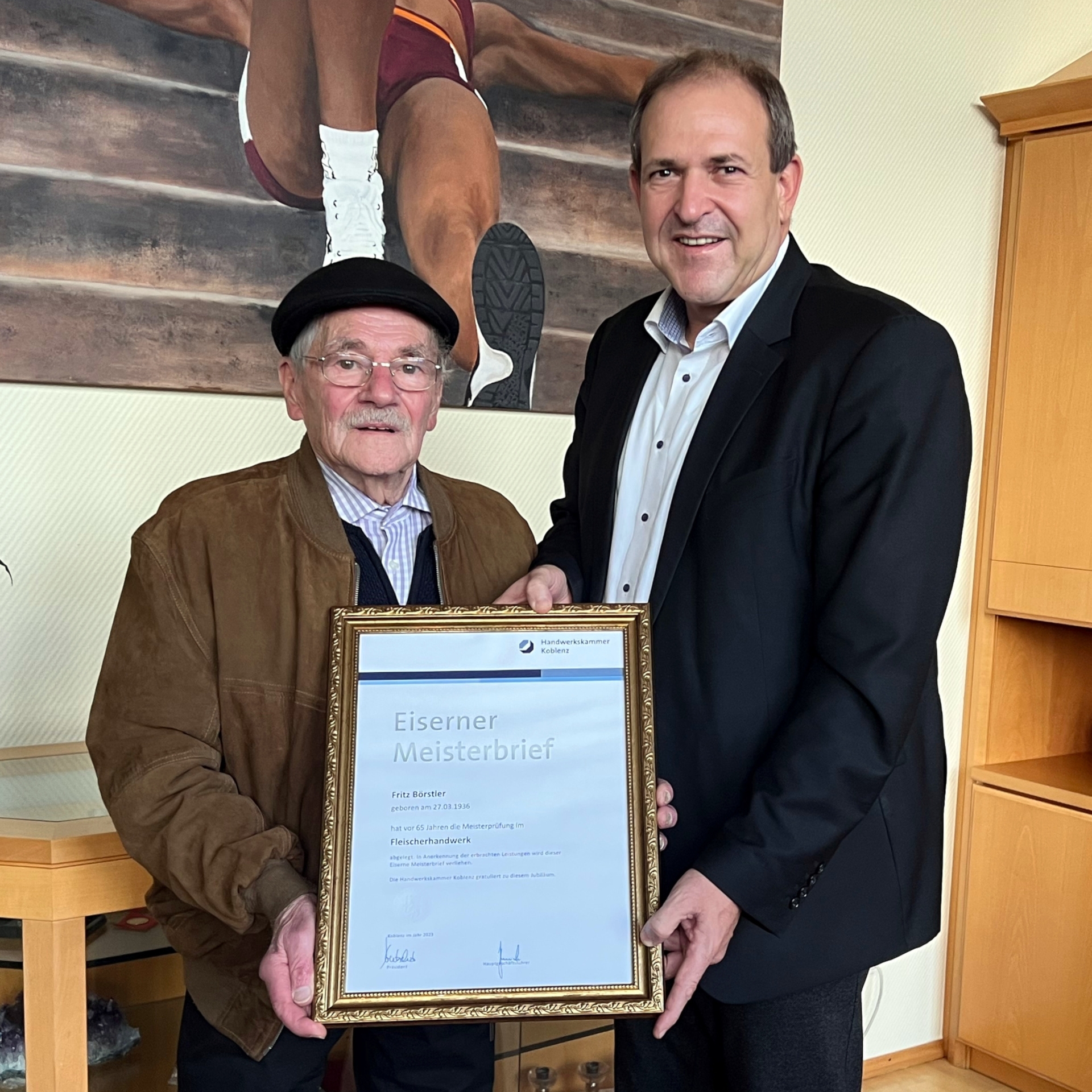 La photo montre Fritz Börstler et le maire Frank Frühauf. Ils se tiennent côte à côte dans le bureau du maire et tiennent le diplôme de maître de fer face à la caméra.