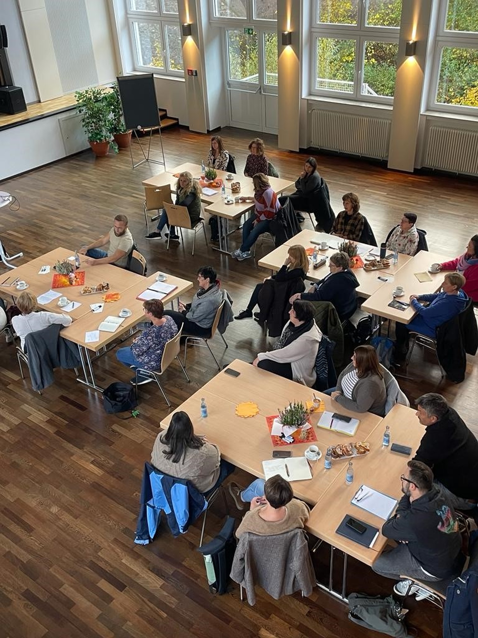 La photo montre une vue d'en haut des participants à la conférence dans l'aula Göttenbach. Ils sont assis à plusieurs tables.