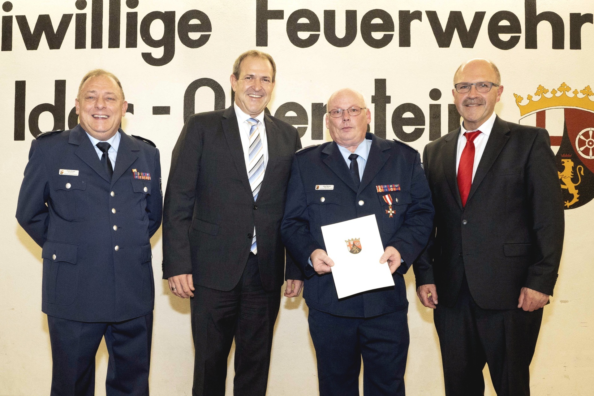 La photo montre le chef de garde adjoint Frank Knapp, le maire Frank Frühauf, le chef de la défense Jörg Riemer et le maire Friedrich Marx, debout côte à côte sur la scène. Jörg Reimer tient un certificat dans la main.