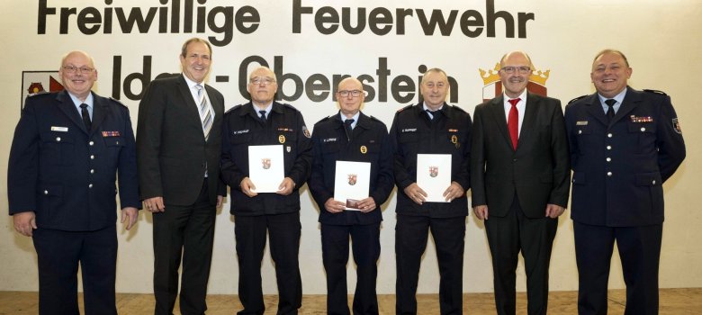 La photo montre les trois personnes honorées sur scène avec leurs diplômes. Ils sont entourés des deux chefs de corps et du conseil municipal. - Link öffnet seitenüberlagerndes Dialog-Fenster