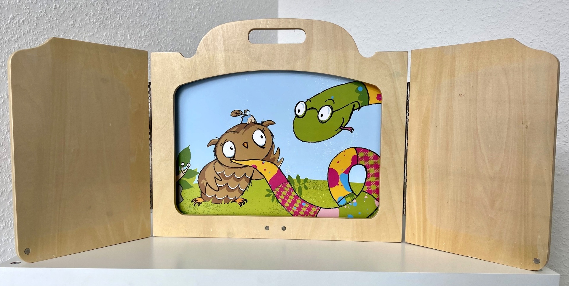 La photo montre un cadre Kamishibai en bois. Il est posé sur une table et le cadre contient une carte-image du livre "Le hibou avec une bosse".