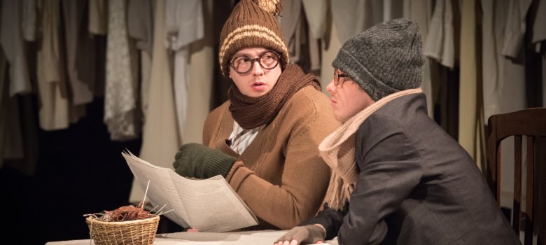 La photo montre deux acteurs assis à une table avec des vestes d'hiver et des bonnets.
