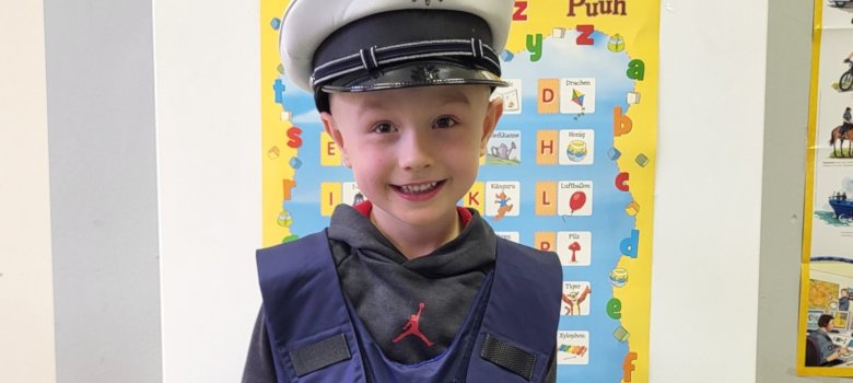 La photo montre un enfant photographié avec une casquette de police et un gilet de protection.