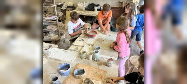 La photo montre les enfants en train de faire de la poterie avec le maître potier Manfred Weigel.