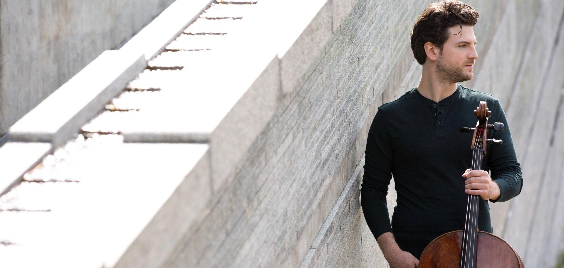La photo montre Gabriel Schwabe, debout devant un mur avec son violoncelle, regardant au loin.