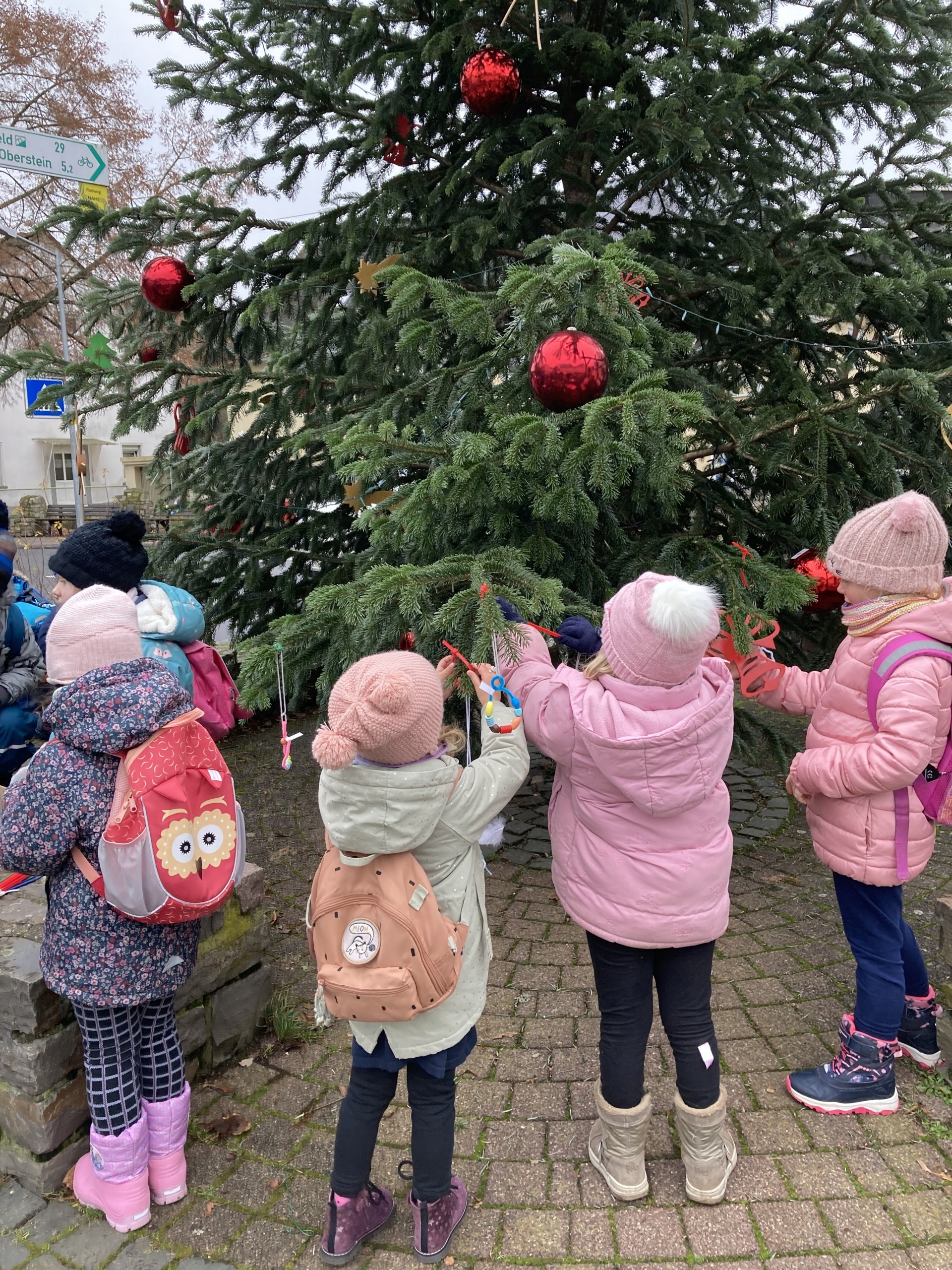 La photo montre quatre enfants en train de décorer le sapin de Noël.