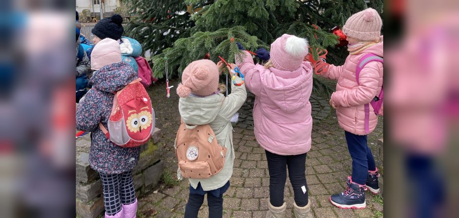 La photo montre quatre enfants en train de décorer le sapin de Noël.