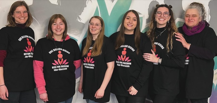 La photo montre les six femmes de l'équipe organisatrice, vêtues de T-shirts uniformes, debout côte à côte devant un mur et souriant à la caméra.