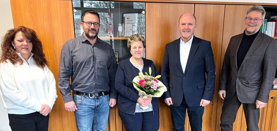 La photo montre, de gauche à droite, la présidente du comité du personnel Susanne Becker, Christoph Alt du service de gestion des bâtiments, Irene Herrherdt, le maire Friedrich Marx et le chef de bureau Wolfgang Petry. Ils se tiennent devant une armoire murale et regardent la caméra, Mme Herrherdt tenant un bouquet de fleurs dans les mains.