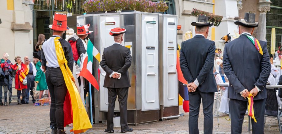 La photo montre des personnes déguisées se tenant à l'extérieur sur une place devant des toilettes.