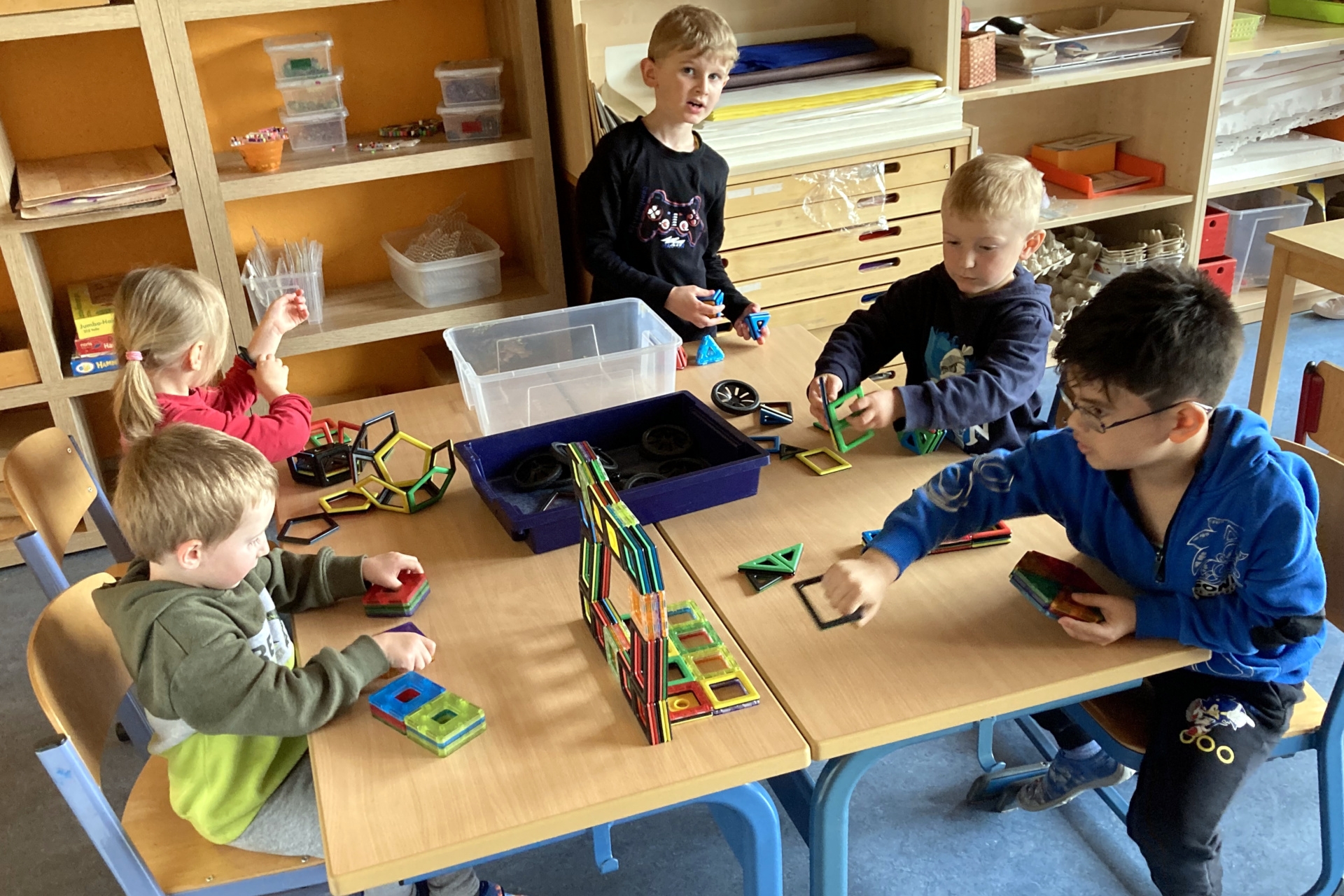La photo montre des enfants assis à une table et jouant avec des blocs de construction magnétiques.