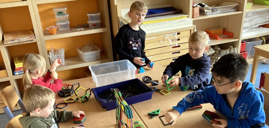 La photo montre des enfants assis à une table et jouant avec des blocs de construction magnétiques.
