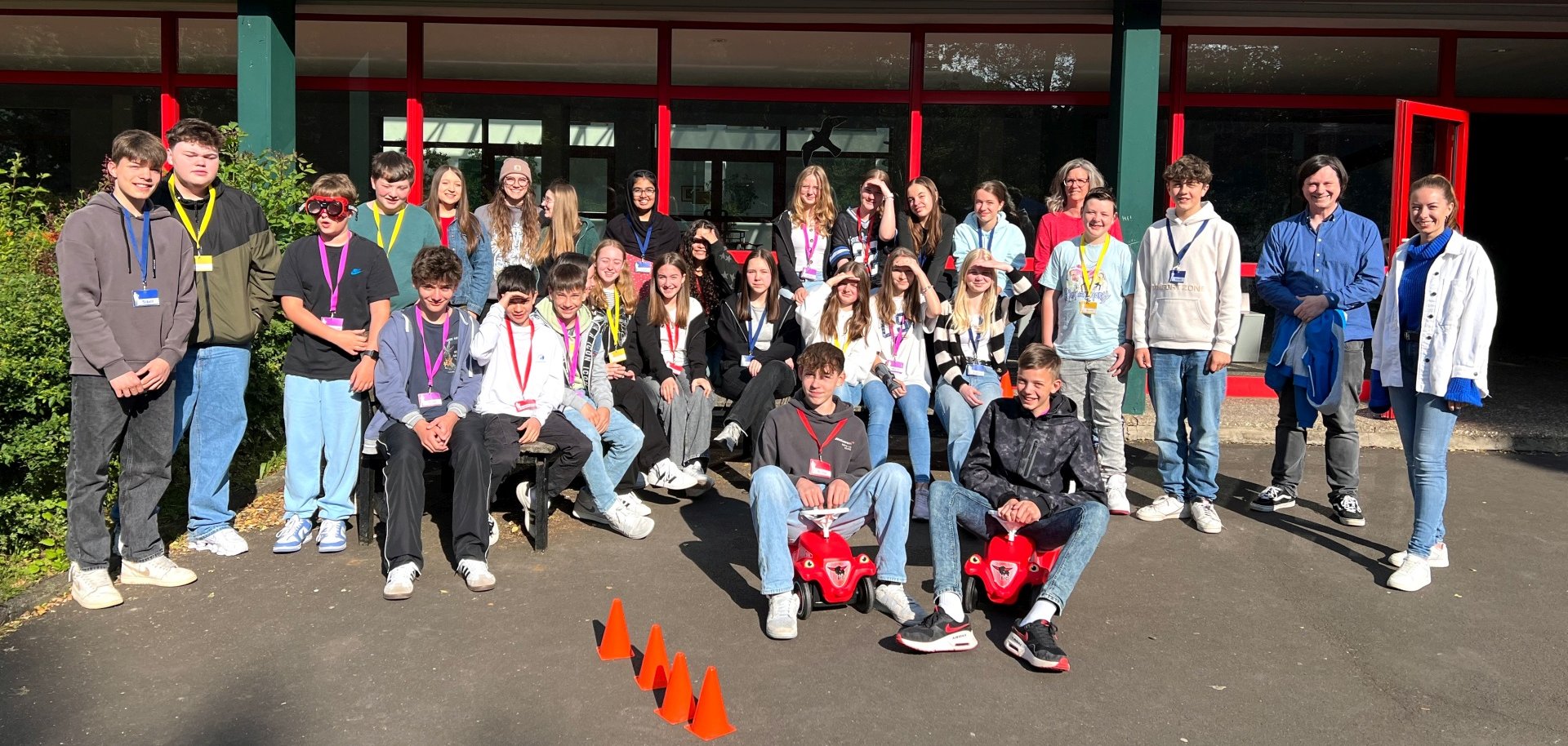 La photo montre les élèves et le personnel du service municipal de la jeunesse. Ils se tiennent ensemble devant le bâtiment scolaire et regardent la caméra.