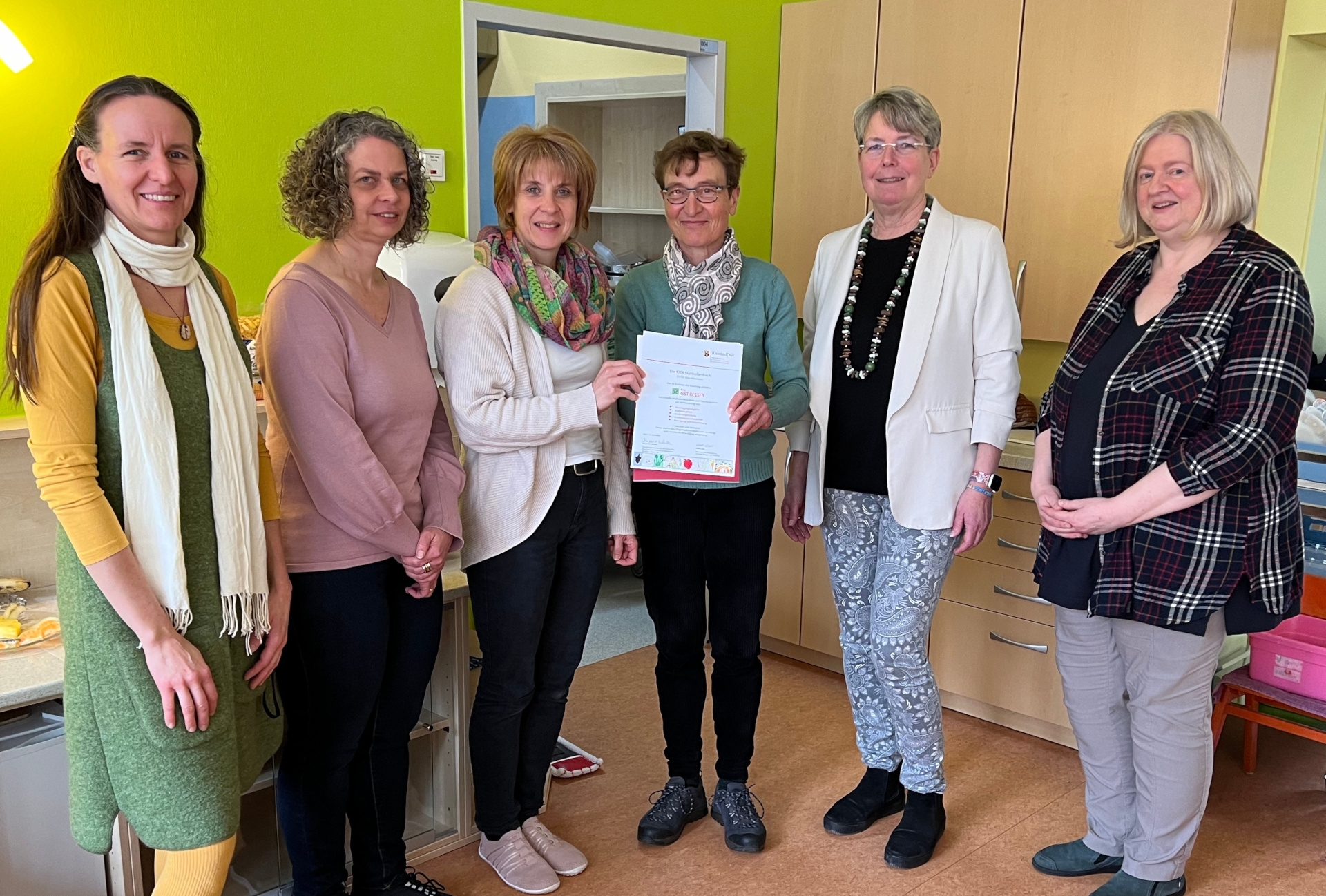 La photo montre les acteurs du projet lors de la remise du certificat à la directrice de la crèche Silke Fritsch par Irmgard Lüttiken. Avec elle, Silke Fritsch (3e à partir de la gauche) se réjouit. Tina Weber, Anja Pullem, Katrin Schwarz et Juliane Groß, conseillère spécialisée pour les crèches, se sont réjouies avec elles.