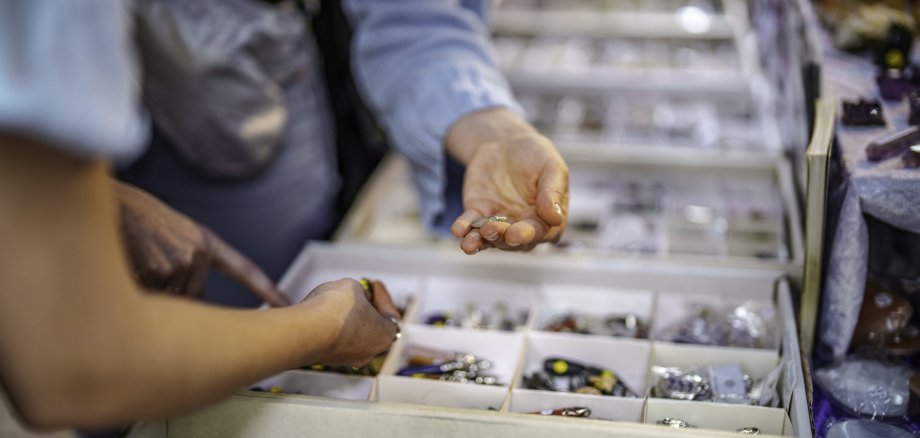 La photo montre une vue de l'étalage d'un magasin de pierres précieuses. On y voit les mains de deux clients saisissant des pierres.