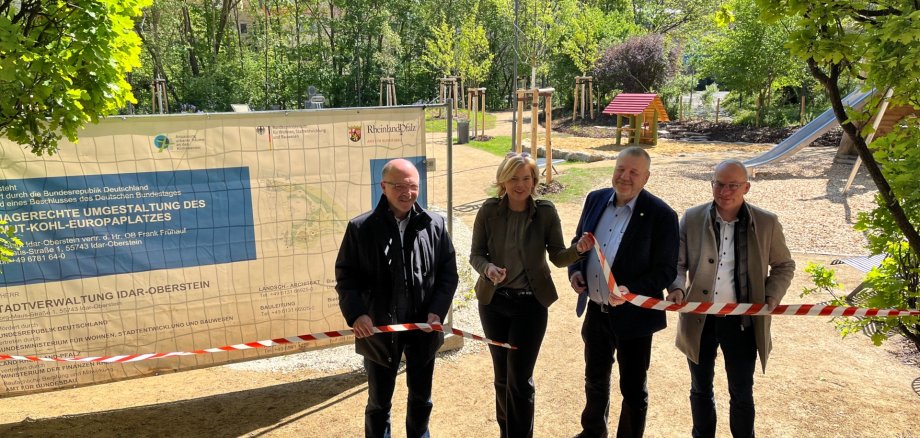 La photo montre les personnes mentionnées. Elles se tiennent côte à côte derrière un ruban de tracé et regardent la caméra. Julia Klöckner tient une paire de ciseaux et vient de couper le ruban. En arrière-plan, on voit l'installation avec la zone de jeux.