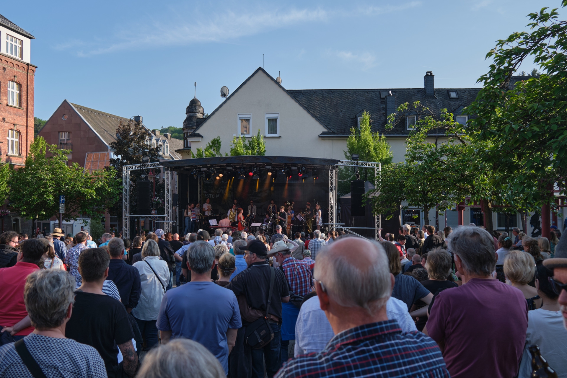 La photo montre en arrière-plan la scène sur la place du marché, devant laquelle on peut voir de nombreuses personnes.