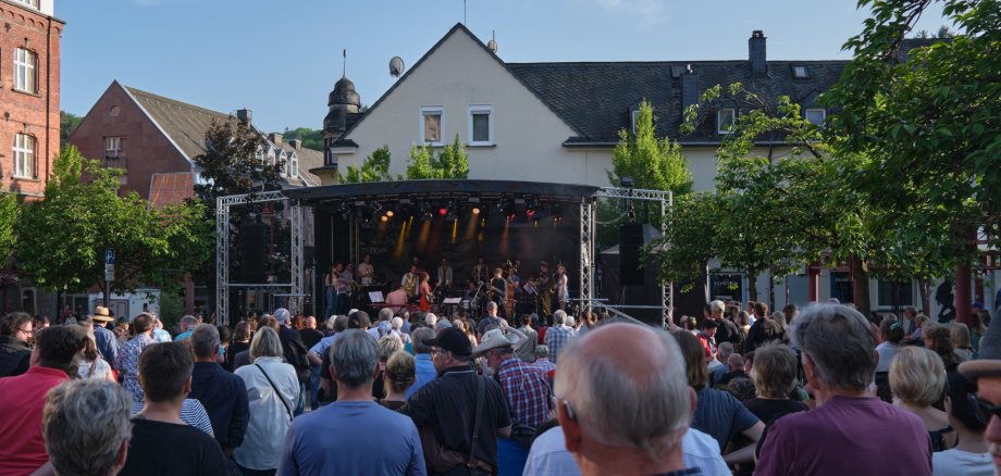 La photo montre en arrière-plan la scène sur la place du marché, devant laquelle on peut voir de nombreuses personnes.