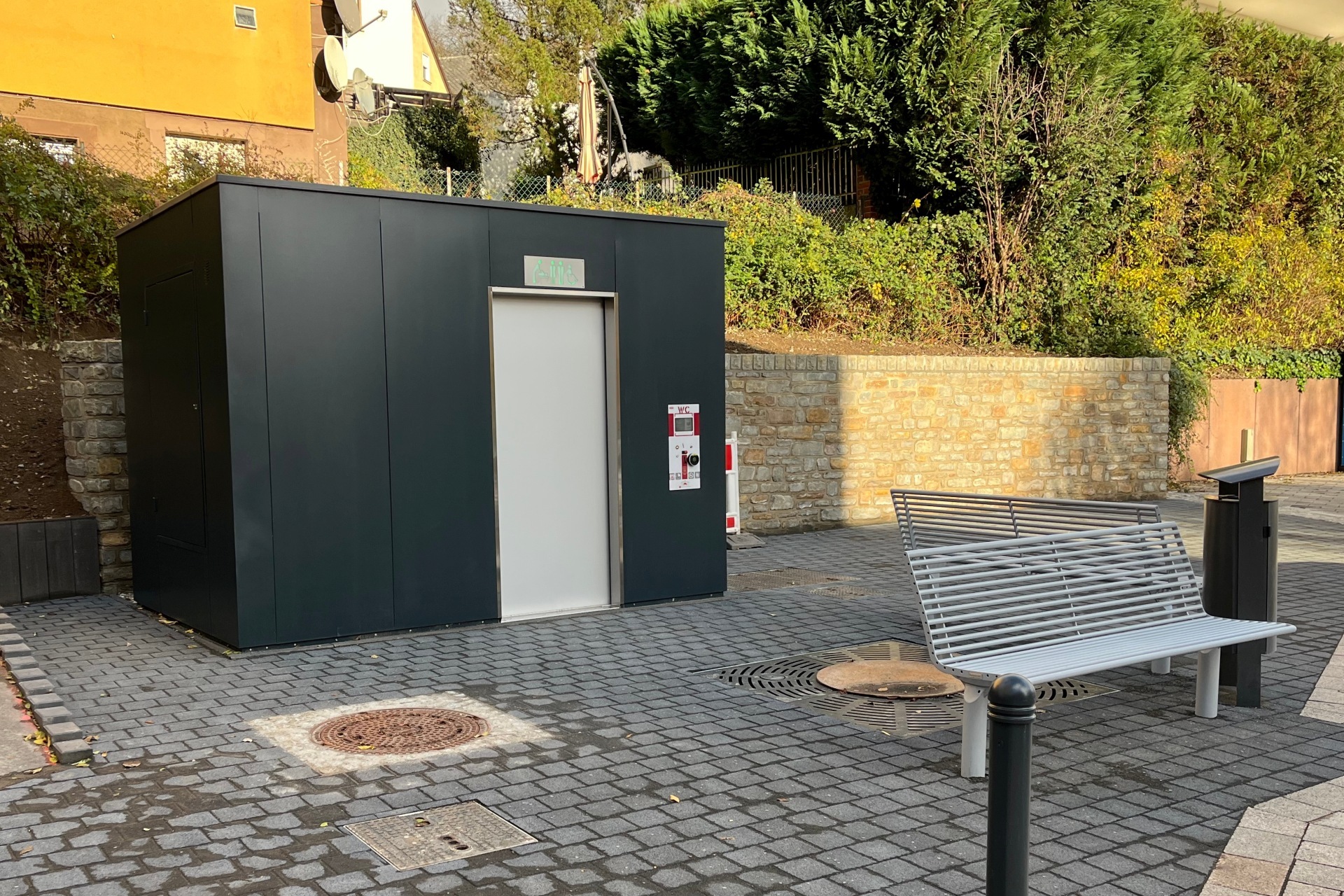 La photo montre la cabine de toilettes et les bancs de repos avec poubelle placés devant.