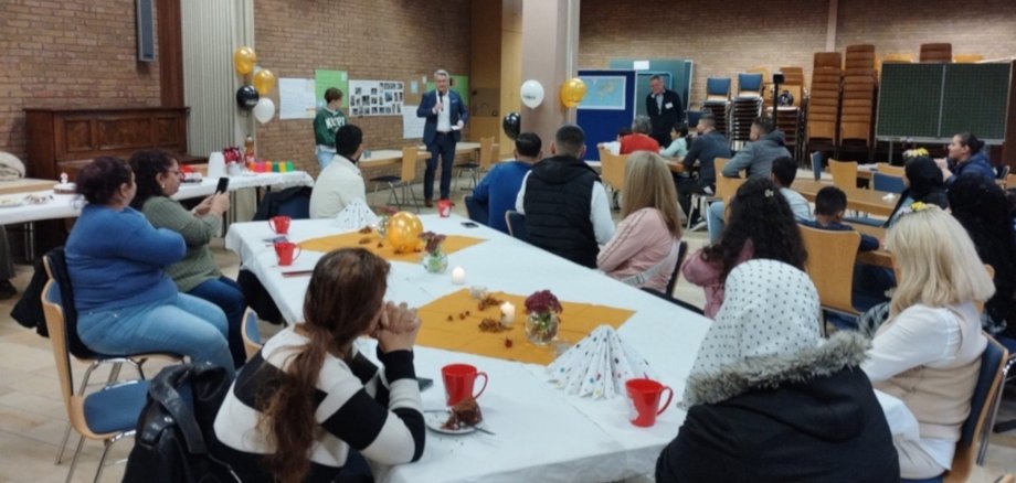 La photo montre de nombreuses personnes assises à des tables. Elles regardent le chef de district Kowalski, qui se tient à l'arrière-plan de la photo et parle dans un microphone.