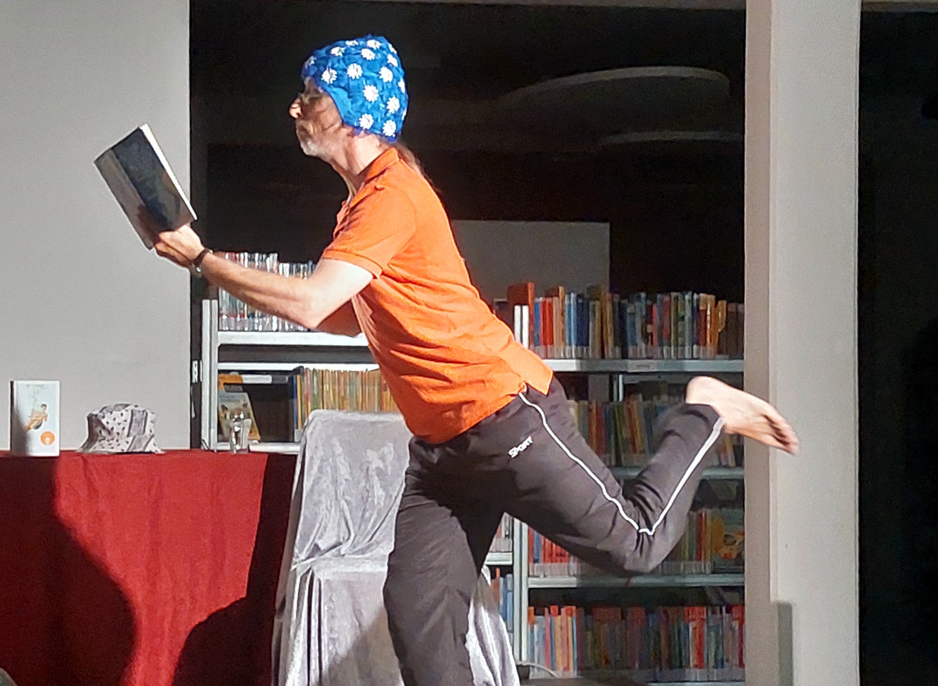 La photo montre Rainer Rudloff de profil, debout sur une jambe, l'autre repliée. Il tient un livre à la main et porte un bonnet de bain sur la tête.